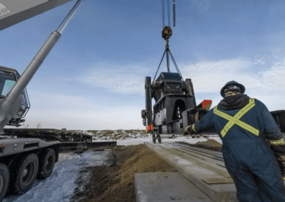 A crane lifts a large vehicle onto a truck, showcasing heavy machinery in action at a construction site.